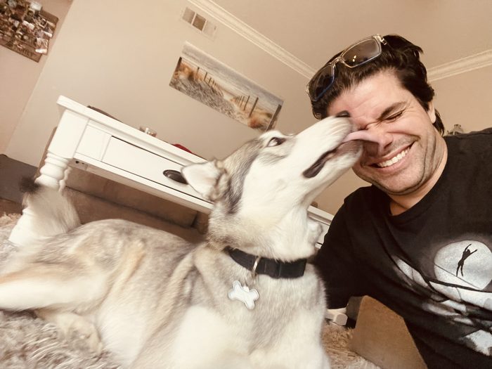 Chad laughing as Finn, a gray and white husky, licks his nose